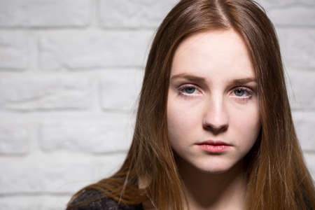 Close shot of bored, long haired and blue-eyed girl's face, at the brick wall backgroundの写真素材