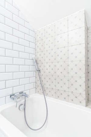 White corner of a minimalist bathroom with brick-resembling tiles and a ceramic bathtub