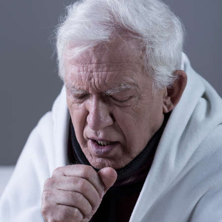Ill coughing senior man covered with blanketの写真素材