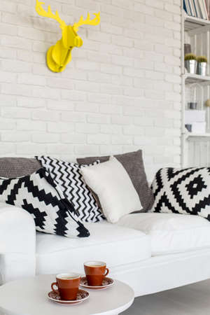 Close-up of a white, comfortable sofa with decorative cushions in a modern living room with white...