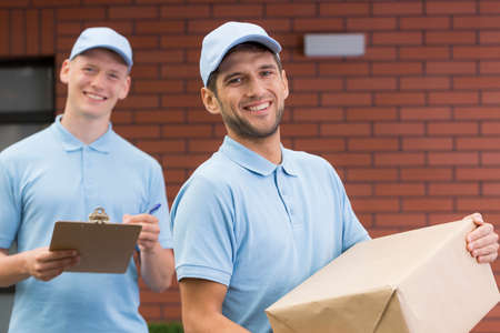 Two post men standing in front of the house with the deliveryの写真素材