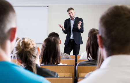 Smiled lecturer is explaining something to his students in a classroom