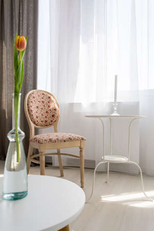 Small table and stylish upholstered chair standing in light living roomの写真素材