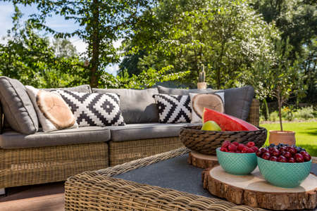 Image of an outdoor rattan sofa and coffee table, trees in the backgroundの写真素材