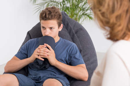 Depressed teenager talking with a mature psychologist, light interiorの写真素材