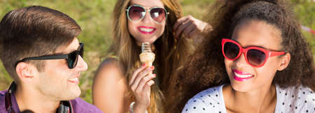 Young people with sunglasses sitting together on a ground with ice cream