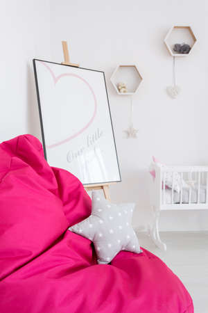 Close shot of a pink bean bag chair with star cushion and baby cradle and easel behindの写真素材