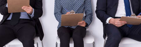 Closer shot of three people sitting close each other on the chairs and making notes