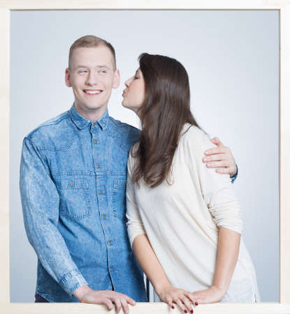 Picture in a white frame of a young woman kissing a happy man in a chick