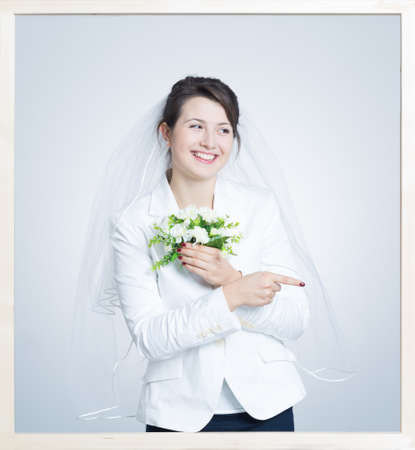 Picture in a frame of a young bride in wearing a veil, holding a small bouquetの写真素材