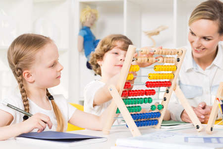 Children in elementary school learning to count on a colourful abacus with the help of their teacherの写真素材