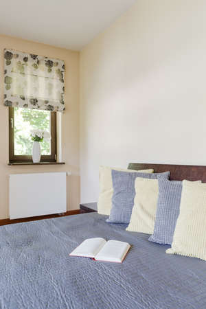 Corner of a creamy bedroom with a large bed covered with blue bed spread in the foreground