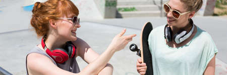 Two happy female friends spending time at skate park during summer day, panorama