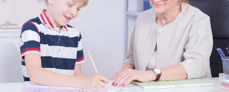 Close-up of a smiling schoolboy doing his homework assisted by a tutor