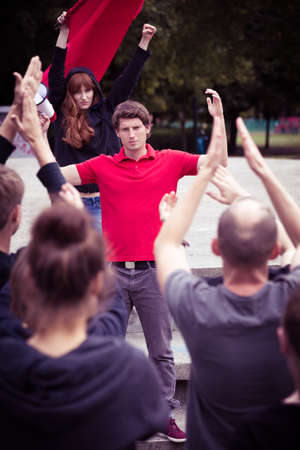 Young leader of a demonstration standing with raised arms before the crowd of peopleの写真素材