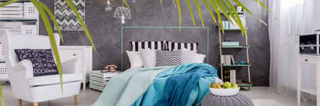 Modern bedroom interior with comfortable armchair, marital bed and blue blanket