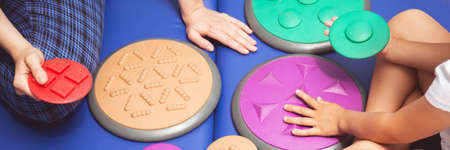 Child during sensory integration therapy touching a colorful tactile disc, panorama