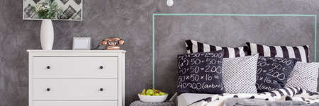 Shot of a white commode close to the head of a bed full of pillows
