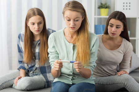 Terrified teenage girl holding a pregnancy test and her two friends