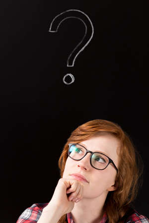 Portrait of pensived woman with glasses with question mark at black backgroundの写真素材