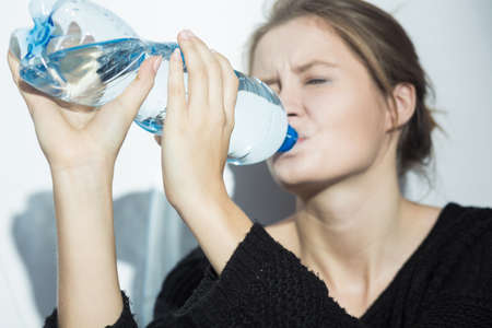 Shot of a woman drinking water from the bottle kept both hands