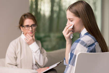 Mature psychotherapist looking at her crying teenage parient