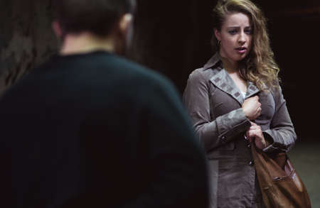 Terrified woman holding her bag, dangerous thief behind herの写真素材