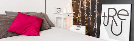 Closeup of a bed, fairy lights hanging on a wall and a framed posterの写真素材