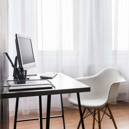 Light interior with desk, chair and sofa. Modern room with white curtain and flooring.