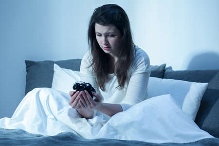 Shot of a young woman sitting on her bed and holding an alarm clockの写真素材