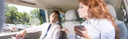 Red-haired woman sitting in a car with the mobile phone and talking to the elegant man