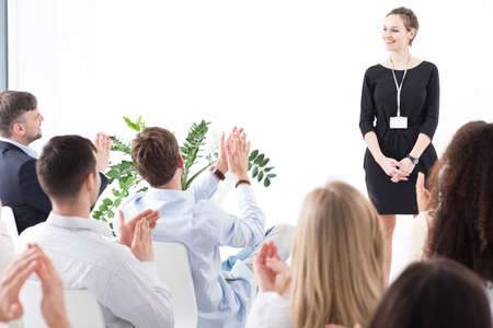 Happy corporation worker standing in front of her colleagues who are applauding her