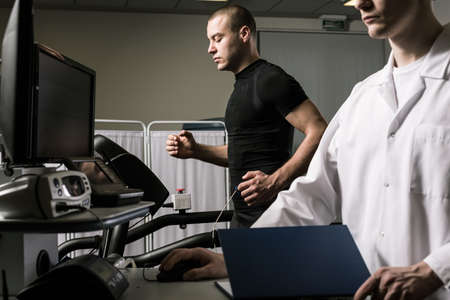 Shot of a man running on a treadmill with electrode attachted to his body and a young doctor
