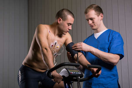 Shot of a man sitting on a stationary bike and looking at his arm while medic is checking his blood...