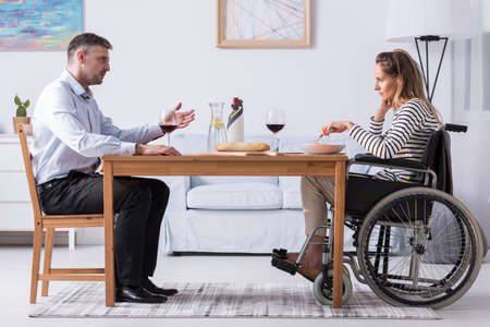 Husband talking to her unhappy disabled wife during dinner at homeの写真素材
