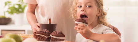 Happy little boy is trying to bite muffin prepared by his grandmotherの写真素材