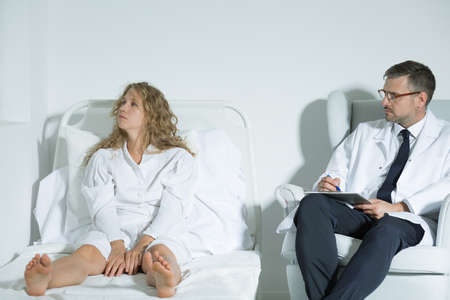 Shot of a psychiatrist trying to talk to his patient sitting on a bed and not looking at himの写真素材
