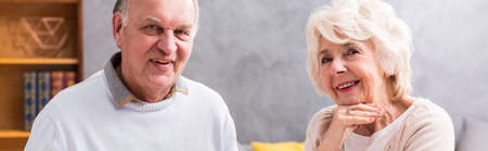 Panoramic portrait of a happy senior marriage sitting together in a grey interiorの写真素材