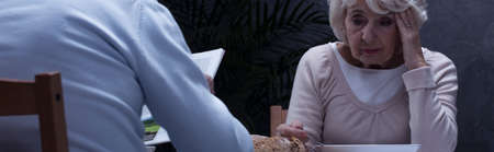 Panorama of a very upset elderly lady sitting opposite to her husband at a table and eating a soupの写真素材