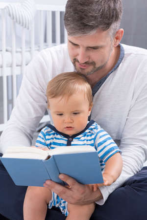 Shot of a men holding a baby and reading a book to himの写真素材