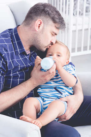 Shot of a father kissing his baby on a forehead and feeding him with a bottleの写真素材