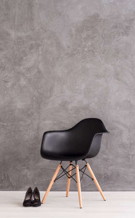 Black minimalistic chair on a cyan wall background with black high heels on the floorの写真素材