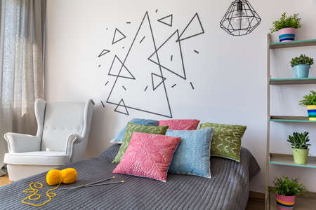 Cropped shot of a stylish bedroom interior with a white armchair and colorful pillows on a bed