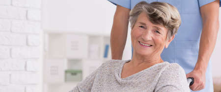 Close shot of smiled woman on a wheelchair with her caregiver standing behindの写真素材