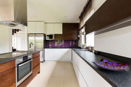 Shot of a spacious modern kitchen with white and brown furniture and violet details