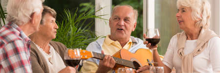 Elder man playing the guitar with his friends singing a songの写真素材