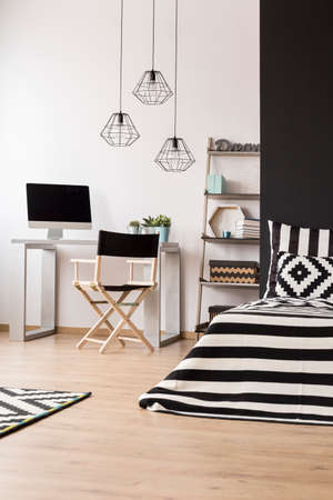 Black and white home interior with bed, pendant lamp, chair, desk and computerの写真素材
