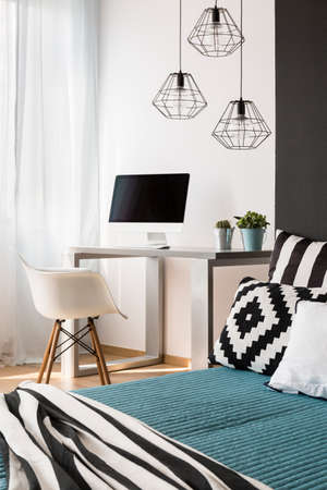 Light room with bed, chair, computer, desk and modern pendant lampsの写真素材