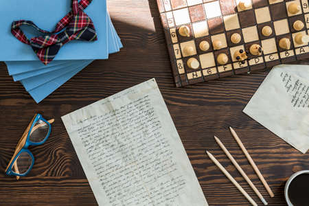 Wooden desk with books, chess play, notes, pencils and glasses on