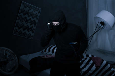 Burglar wearing black clothes holding a flashlight breaking into a house at nightの写真素材